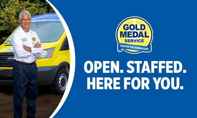 A smiling technician in front of a Gold Medal van with text reading open, staffed and here for you.