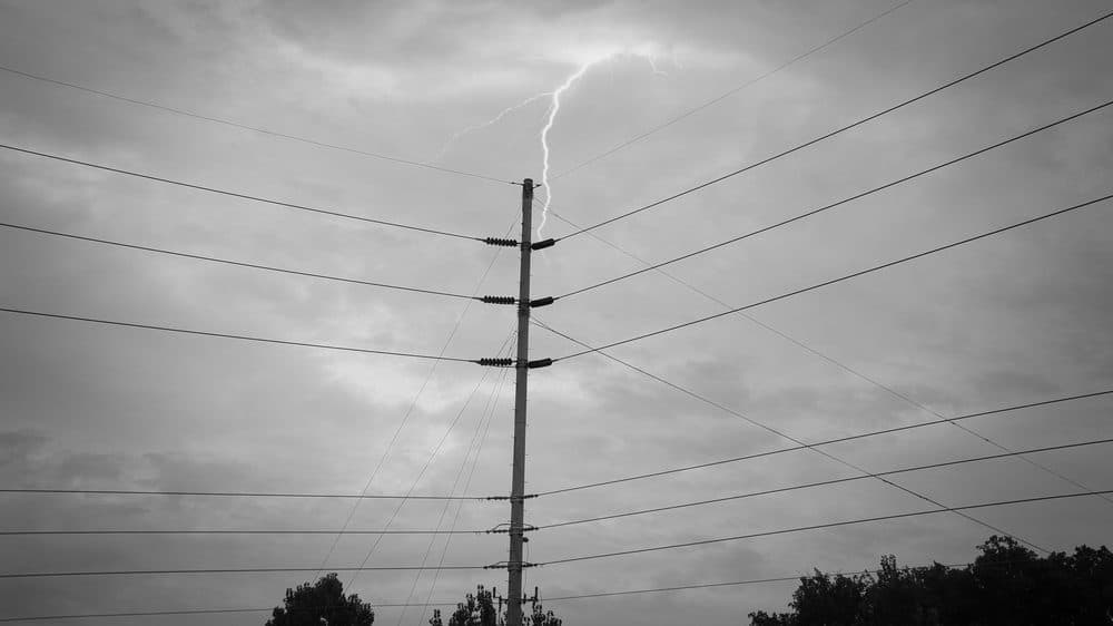 A lighting strike is seen in the background behind a power pole and power lines