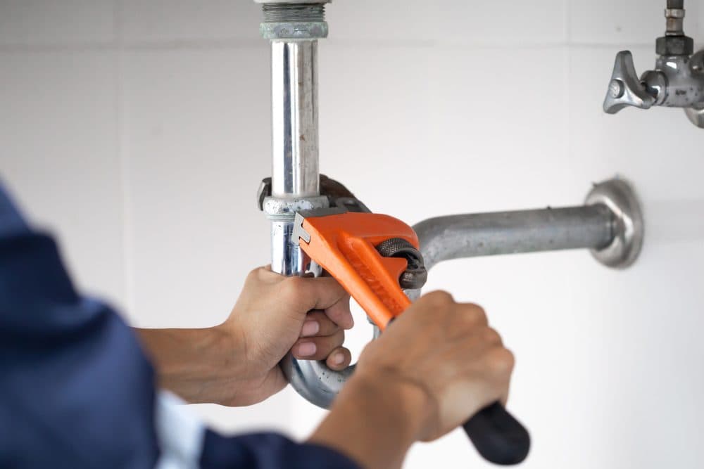 A technician is using a pipe wrench to adjust a pipe with both hands