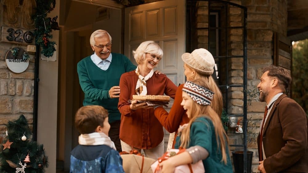 Grandparents greeting a woman, man, and two children at the front door with everyone dressed in their holiday best