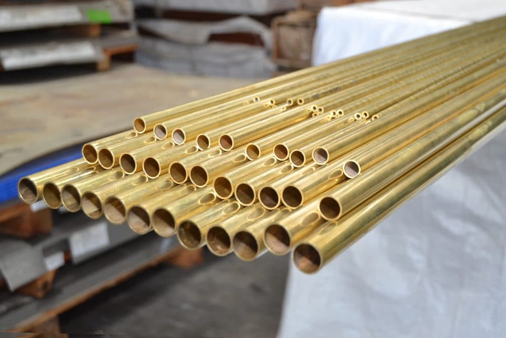 Four different sizes of brass plumbing pipes stacked on top of each other from largest diameter to smallest diameter
