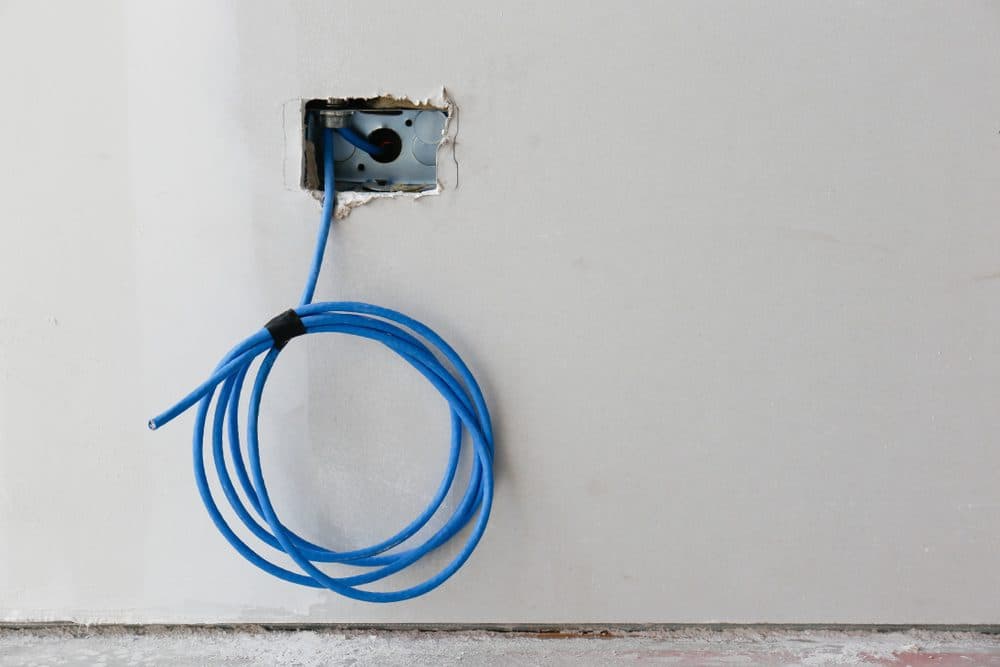 A spool of blue wiring hanging out of sheet rock