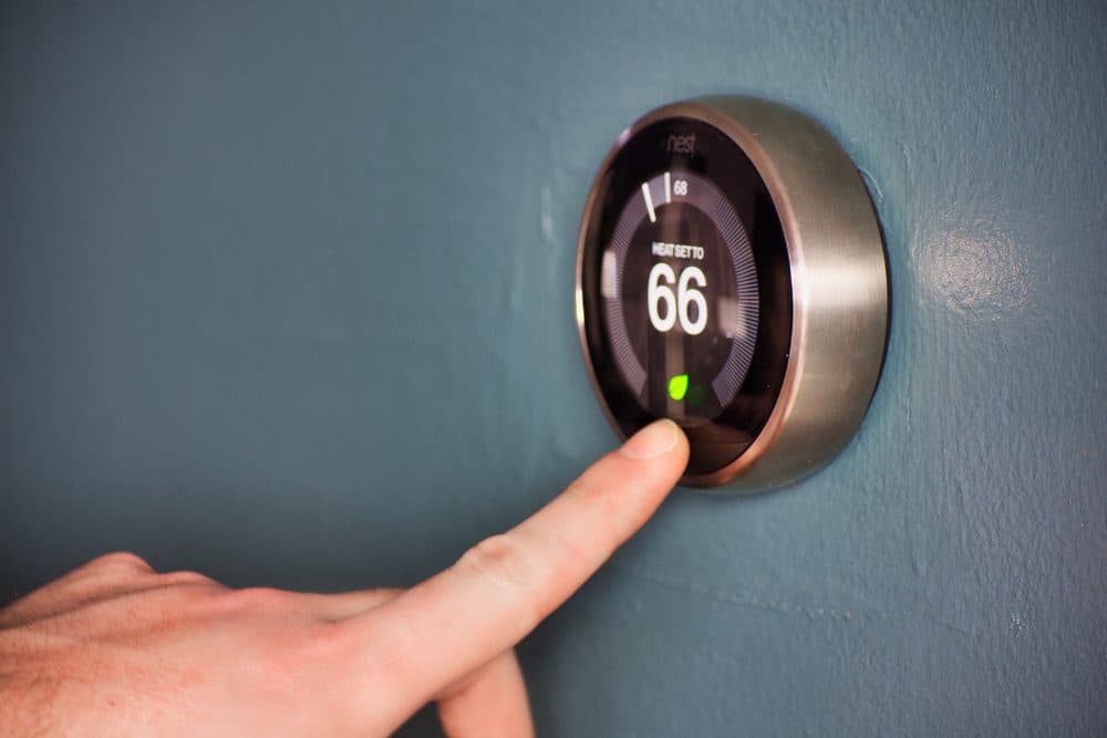 A left index finger is adjusting a smart thermostat's temperature screen