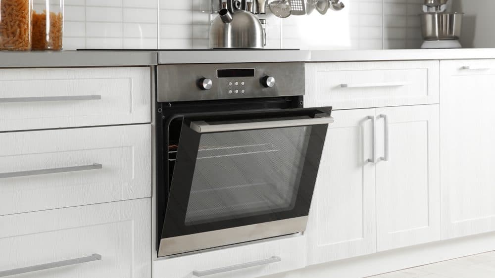 A slightly ajar stainless steel oven in an all-white kitchen