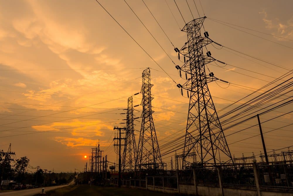 Three electrical towers with an orange, cloudy sunset in the background