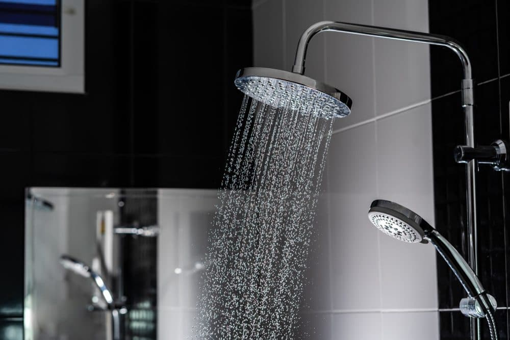 Rain shower head streaming water into a gray tiled shower