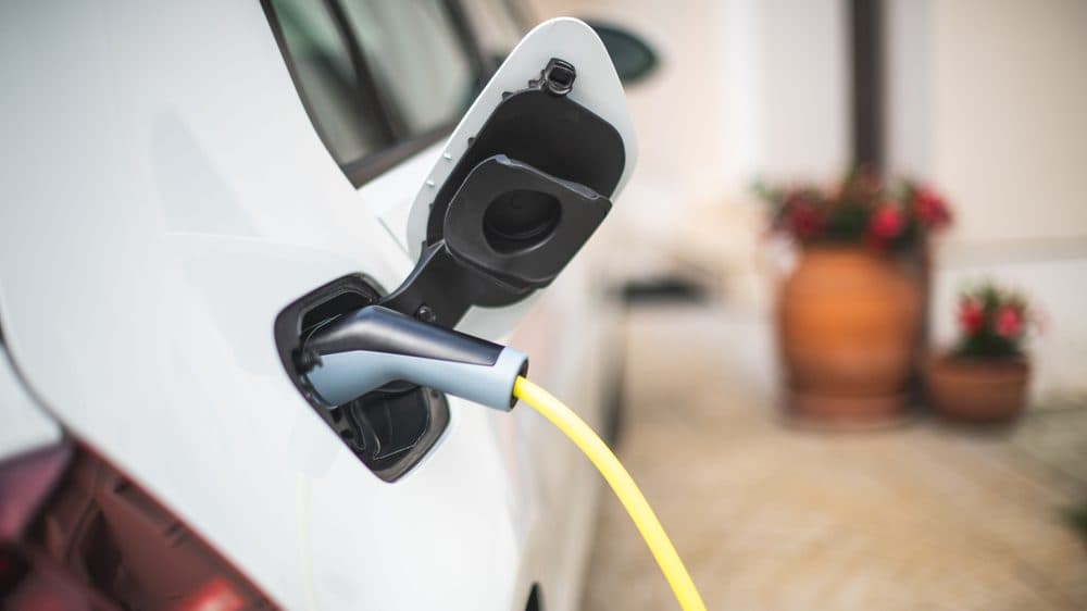 A charging cord is plugged into the back passenger side of a vehicle in a drive way