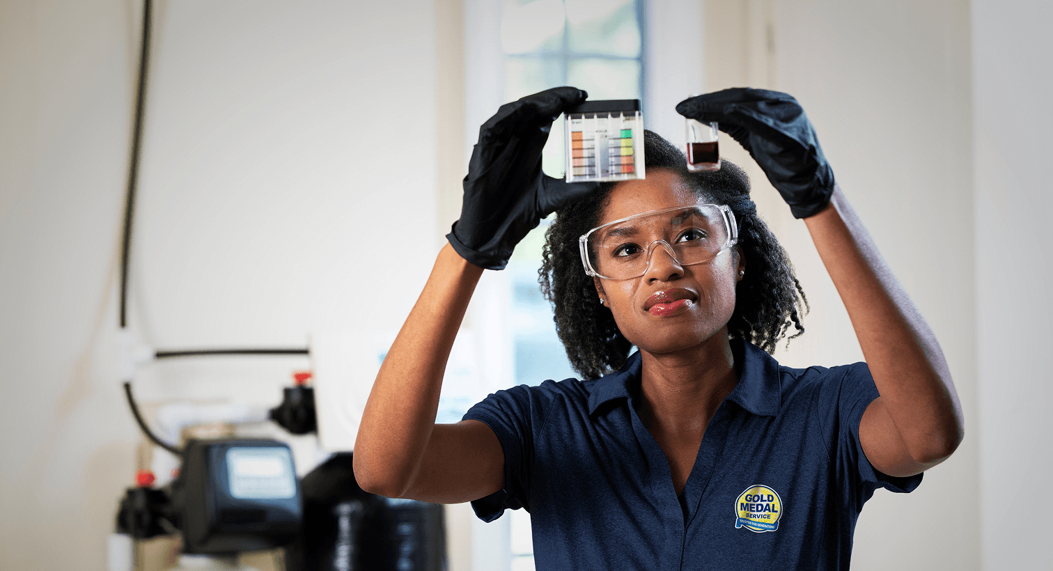 A professional Gold Medal technician conducting a home water quality test next to a residential water treatment filtration system.