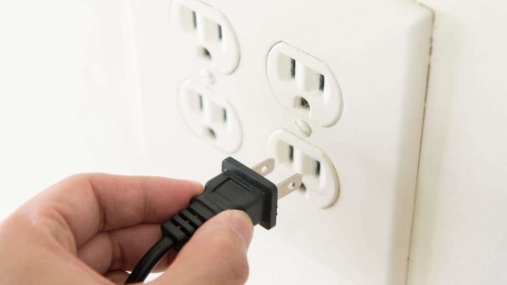 A hand is plugging a power plug into a power outlet