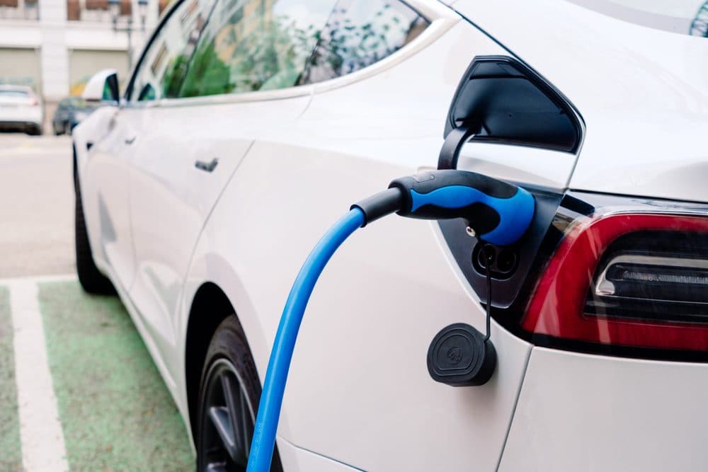 A white vehicle in a parking spot has a blue charging cord plugged into it
