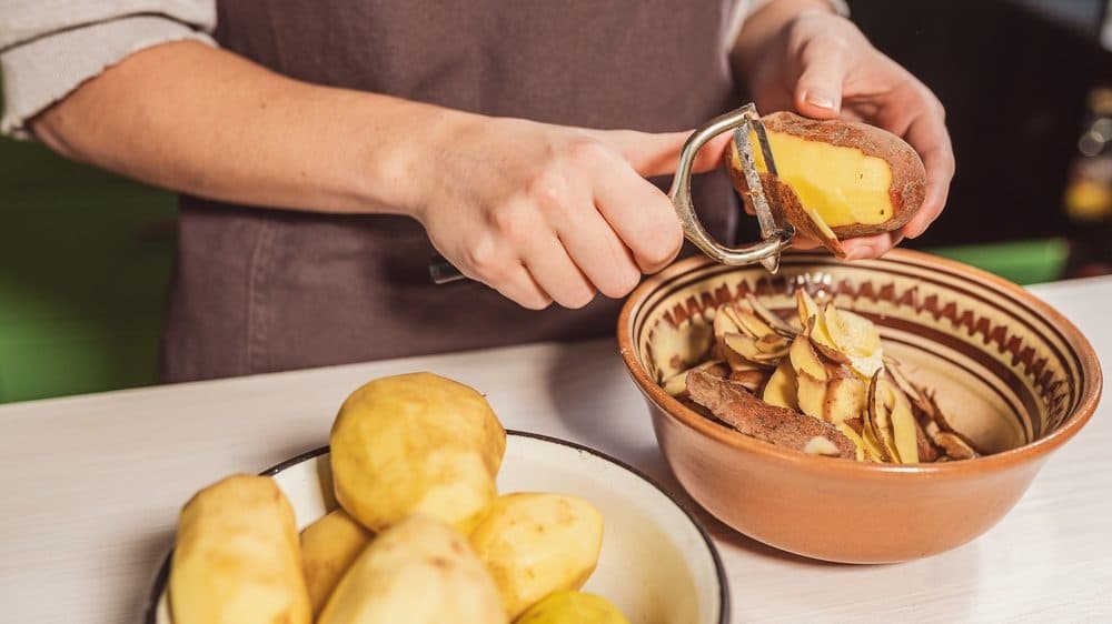 A cook is seen wearing an apron while peeling potatoes into bowls