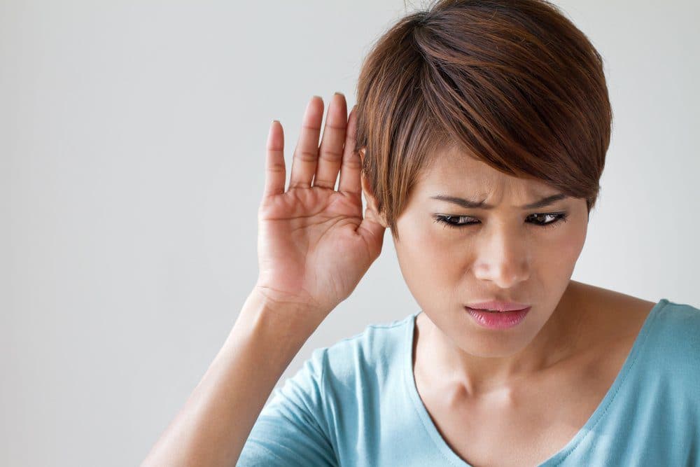 Woman wearing a blue shirt with her hand to her ear trying to listen to something