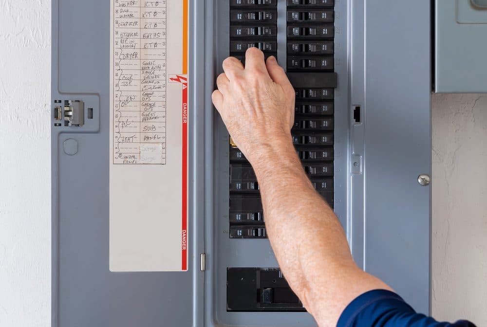 A hand is shown flipping off a circuit breaker inside of a panel