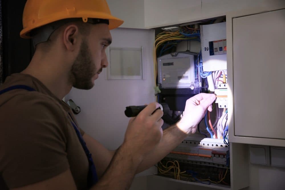 A technician using a flashlight while looking into a circuit breaker panel