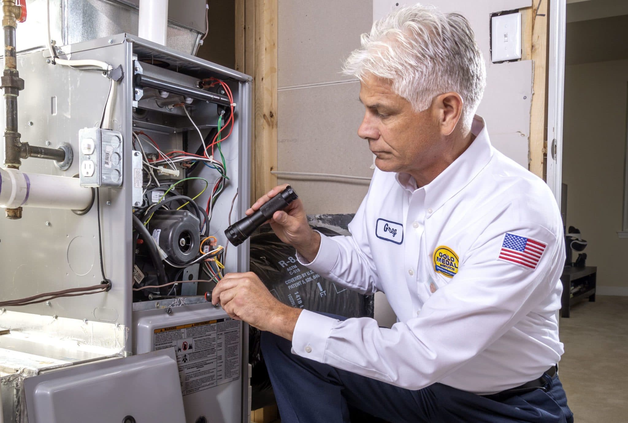 A Gold Medal technician using a flashlight to see into a furnace while performing a tune-up