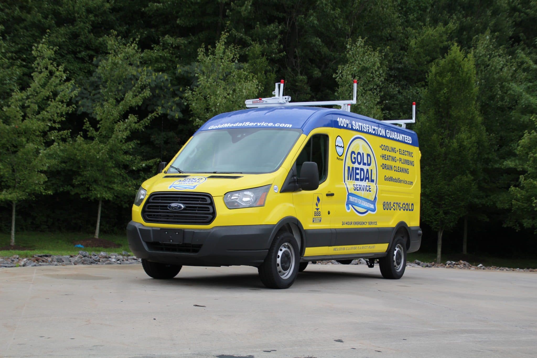 A Gold Medal van sitting in a parking lot with a forest of trees behind it